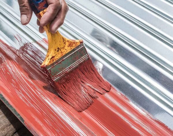 Painting the surface of a sheet of Galvanized Iron or GI corrugated metal with rust inhibiting red oxide primer.